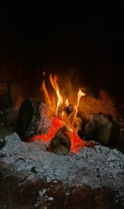 A warm, cozy indoor fireplace with logs burning and glowing embers, perfect for winter ambiance.