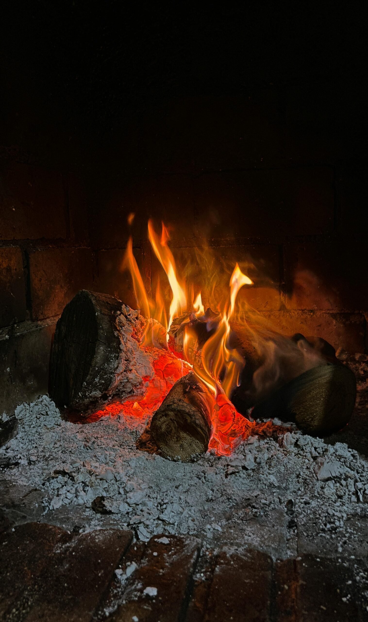 A warm, cozy indoor fireplace with logs burning and glowing embers, perfect for winter ambiance.