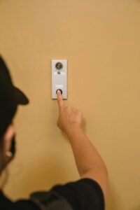 Close-up of a person pressing a doorbell on a beige wall, emphasizing hand action.